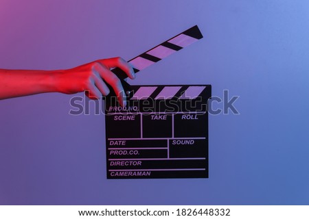 Hand holding film clapper board in blue red neon light. Cinema industry, entertainment.