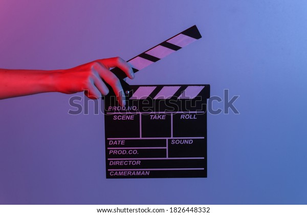 Hand holding film clapper board in blue
red neon light. Cinema industry,
entertainment.