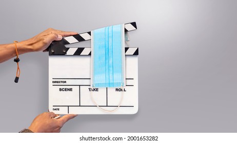 Hand Holding Film Slate With The Protective Face Mask. Its Uses In Film, Movies Production, And The Cinema Industry. Impact Of The Movie Industry From The COVID-19 Pandemic.