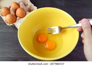 Hand Holding Fork Going To Beat A Pair Of Raw Eggs In A Mixing Bowl