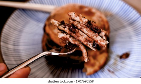 Hand holding a fork spinning slowly with cut pancakes on it.  Plate of pancakes in the background. - Powered by Shutterstock