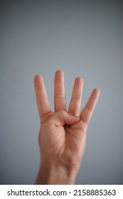 Hand Holding Up Four Fingers Against Blue Grey Background.