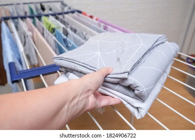 Hand Holding Fresh Washed Bed Linen Stacked, Piled On A Dryer, Dry Apparel On A Folding Portable Dryer Close Up, Housekeeping, Homework And Chores Concept.