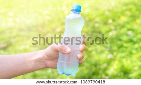 Hand holding fresh water bottle in the park, close up male hand holding water at summer green park outdoor and bokeh nature background, healthy concept, thirst in the heat, balance of water in body