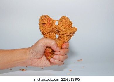 hand holding fried chicken thigh on white background. closeup view