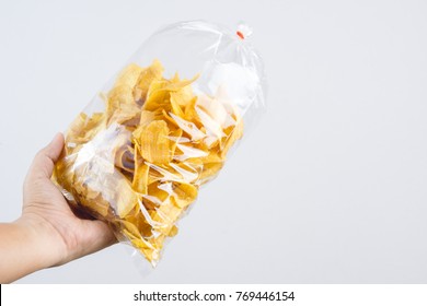 Hand Holding Fried Sliced Banana Chip In Food Plastic Bag Tied By Rubber On White Background