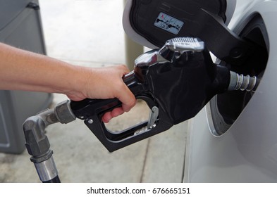 Hand holding gas pump inserted into gas tank of a car