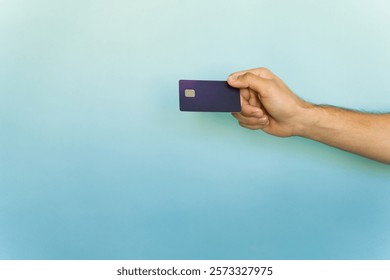 Hand holding a generic mock credit card against a soft gradient light blue background, representing modern finance and digital transactions