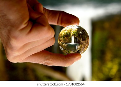 A hand holding a glass ball with a reflection of the Banias watterfall in the north of Israel