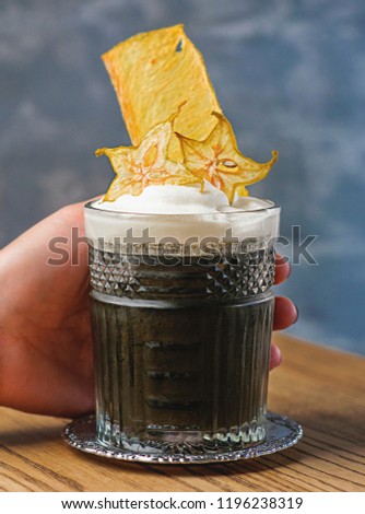 hand holding glass with black cocktail of cuttlefish ink, alcohol, cream with carom
