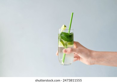 Hand holding glass with iced refreshing mojito cocktail drink on light blue neutral background with empty copy space. - Powered by Shutterstock