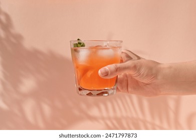 Hand holding glass with iced summer refreshing drink with peach fruits and ice, on pastel peachy pink background with natural sunlight shadows, lifestyle. - Powered by Shutterstock