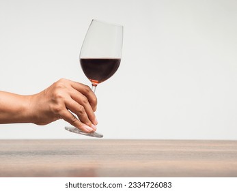 Hand holding a glass of red wine against a gray background. Space for text. Beverage and relaxation concept