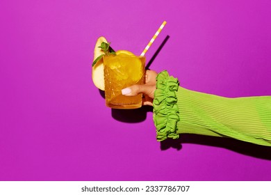 Hand holding glass of screwdriver cocktail with colorful tube over bright studio background. Pop art photoshoot.Copy space for ad. Concept of party, relax, alcohol.