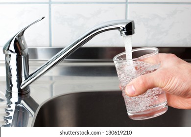 Hand holding a glass of water poured from the kitchen faucet. - Shutterstock ID 130619210