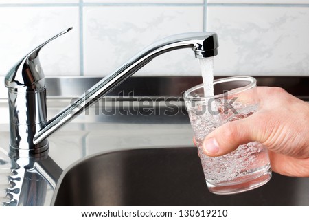 Hand holding a glass of water poured from the kitchen faucet.