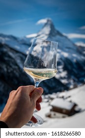 Hand Holding A Glass Of White Wine In Front Of Matterhorn In Winter In A Restaurant