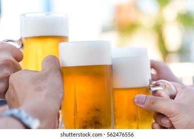 Hand Holding Glasses Of Beer  Clinking Together At Outdoor Resturant