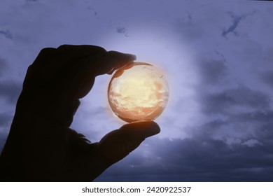 Hand holding a glowing sphere with the sky inside against a dark sky, ray of hope, your world in your hands