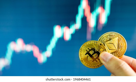 Hand holding gold Bitcoin and Ethereum with blurred candlestick chart in the background. Cryptocurrency and Decentralized finance concept - Shutterstock ID 1968404461