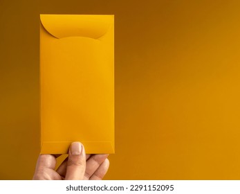 Hand holding a gold envelope, vertical style, isolated on yellow background with copy space. Hongbao packet for lucky money gift in Chinese lunar, new year on January month, exclusive packet.