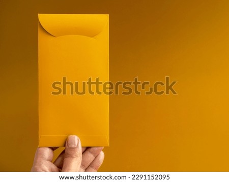 Hand holding a gold envelope, vertical style, isolated on yellow background with copy space. Hongbao packet for lucky money gift in Chinese lunar, new year on January month, exclusive packet.
