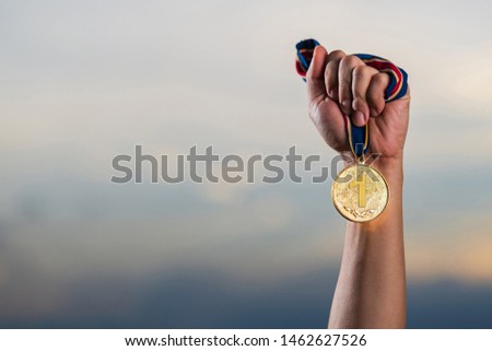 Hand holding gold medal on against cloudy twilight sky background, The winner and successful concept 