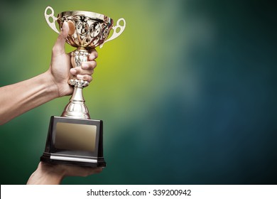 hand holding up a gold trophy cup as a winner in a competition - Shutterstock ID 339200942