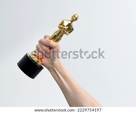 Hand holding golden statuette trophy on white background.