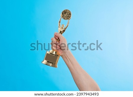 Hand holding golden statuette trophy on blue background.