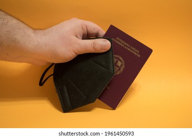 Hand Holding Greek Passport And N95 Facemask For Protection.Travel Restrictions Concept.Travelling During Pandemic.Isolated Over Yellow Background.