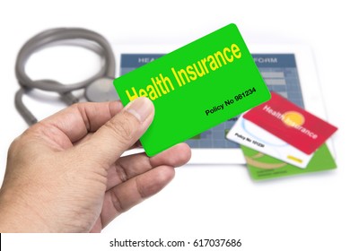 Hand Holding Green Health Insurance Card In Front Of Tablet And Other Insurance Card On White Background.