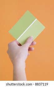 Hand Is Holding Up A Green Paint Sample To An Orange Wall.