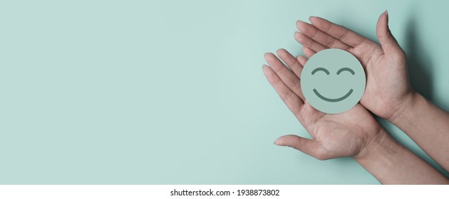 Hand holding green paper cut smile face on green background, positive thinking, mental health assessment , world mental health day concept - Shutterstock ID 1938873802