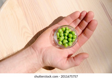 Hand holding green pea in glass bowl of top view on rustic wooden background with copy space, natural wooden table. Flat lay.