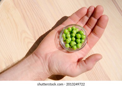 Hand holding green pea in glass bowl of top view on rustic wooden background with copy space, natural wooden table. Flat lay.