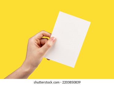 Hand Holding Greeting Card Mockup On Yellow Background. White Empty Paper For Text. Invitation, Letter, Gift, Certificate Template. High Quality Photo