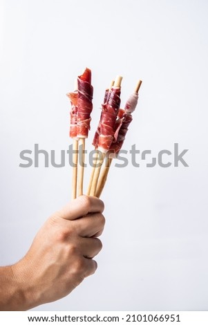 Hand holding grissini with acorn-fed Iberian ham, Spanish tapa, for events, dinners or celebrations,