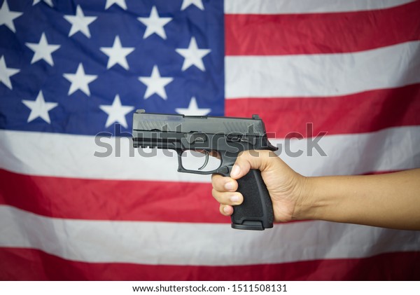 Hand holding\
gun with american flag\
background.