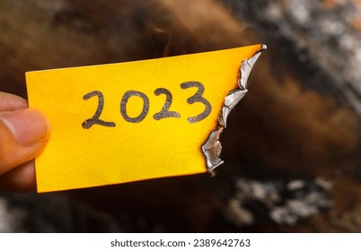 Mano sosteniendo una nota medio quemada con 2023 escrito en ella. nueva vida y concepto de año nuevo 2024. El periódico de 2023 se está quemando, adiós al 2023