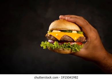 Hand Holding Hamburger On Dark Background.