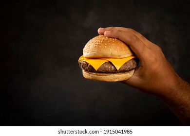 Hand Holding Hamburger On Dark Background.