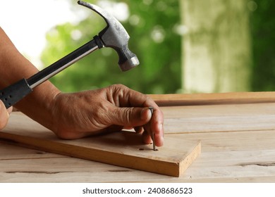 Hand holding a hammer to drive nails into the wood on a tree-blurred background. - Powered by Shutterstock