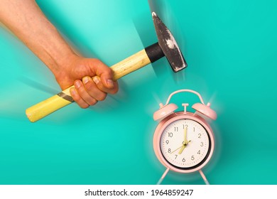 A Hand Holding A Hammer Smashing An Alarm Clock. Blue Background. Killing Time, Time Management And Waking Up Early In The Morning Concept