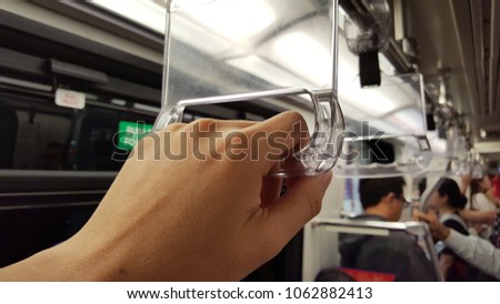 Hand holding a handle in a Mass Rapid Transit (MRT) train or subway with blurred background of passengers.