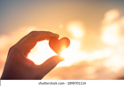 Hand holding heart up to the sun