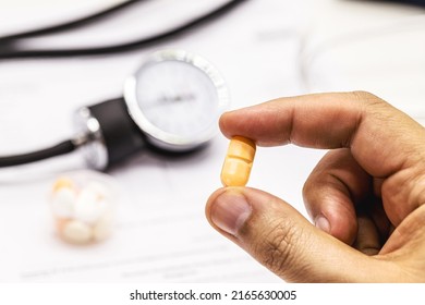 Hand Holding High Blood Pressure Medication, Pill Or Pill, Medical Tests And Sphygmomanometer In The Background