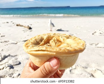 Hand Holding A Hot Meat Pie At The Beach In Jervis Bay National Park With Bird, Sea And Blue Sky On Background.