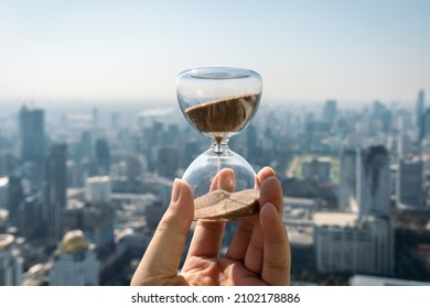 Hand holding a Hourglass with cityscape on panoramic skyline and buildings in the morning background with sun light. The concept of modern life, business, time, management and city life. - Shutterstock ID 2102178886