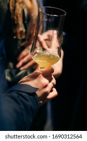 Hand Is Holding A Hurricane Glass With Beer, Tasting Alchohol Drink. Evening Atmosphere, Dark Bar.